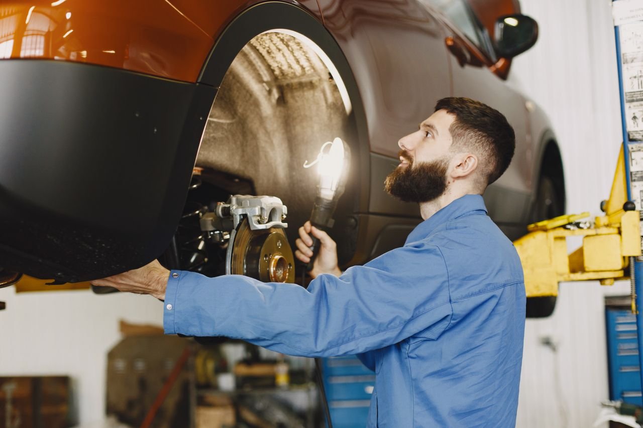 Professional mechanic in blue coveralls inspecting car brakes in a well-lit garage.