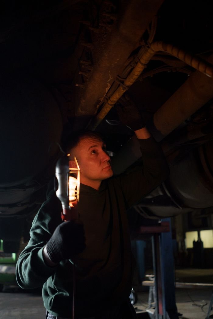 Automotive mechanic using handheld light to inspect a vehicle's underbody in a repair shop.
